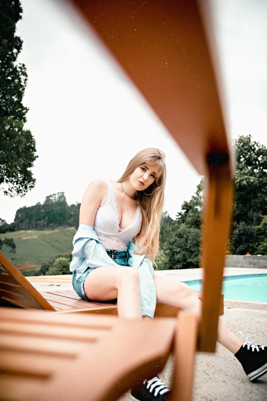 a woman sitting on a deck chair next to a pool, inspired by Elsa Bleda, unsplash, renaissance, portrait of kim petras, open v chest clothes, young beautiful amouranth, low quality photo