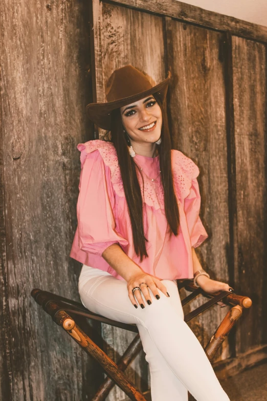 a woman sitting on top of a wooden chair, pink cowboy hat, maya ali, wearing a blouse, smiling down from above