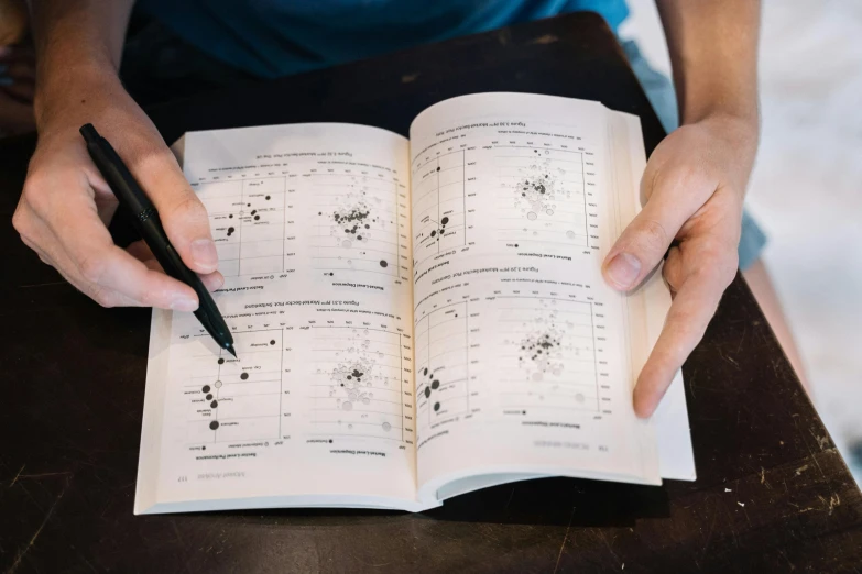 a person sitting at a table with a book and a pen, with a star - chart, interrupting the big game, found schematic in a notebook, thumbnail