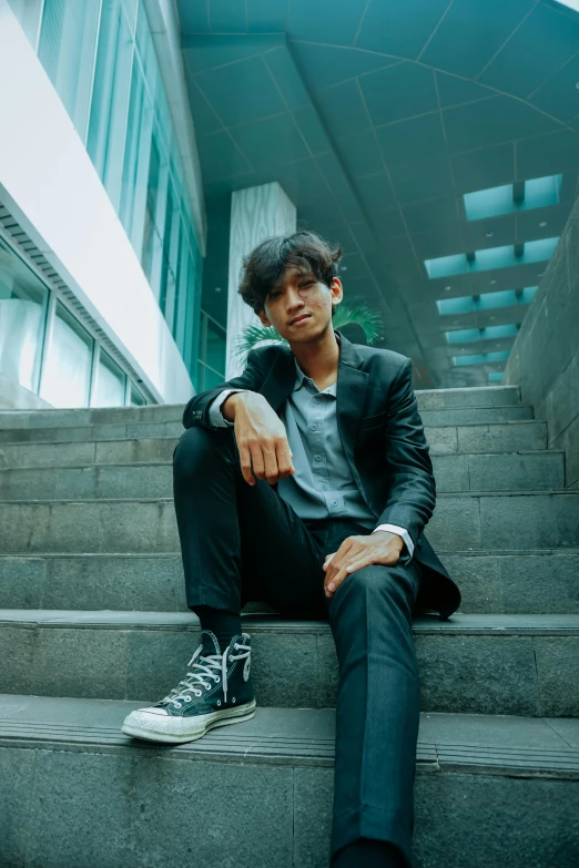 a man sitting on the steps of a building, an album cover, by Basuki Abdullah, pexels contest winner, wearing causal black suits, androgynous person, satisfied pose, indoor picture
