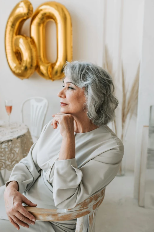 a woman sitting in a chair with balloons in the background, trending on pexels, old gray hair, silver，ivory, celebration, pondering