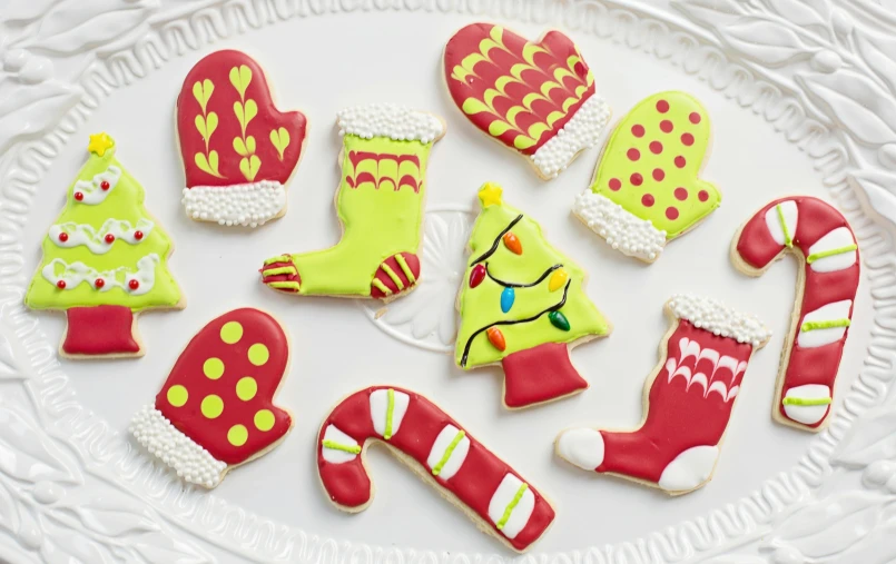 a white plate topped with lots of decorated cookies, inspired by Ernest William Christmas, yellow latex gloves, neon, mittens, olive green and venetian red