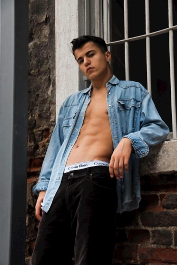 a shirtless man leaning against a brick wall, an album cover, by Cosmo Alexander, trending on pexels, teen boy, double denim, vitaly bulgarov, beautiful midriff