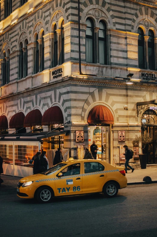 a yellow taxi driving down a street next to a tall building, in the evening, ornate tiled architecture, istanbul, yellow awning