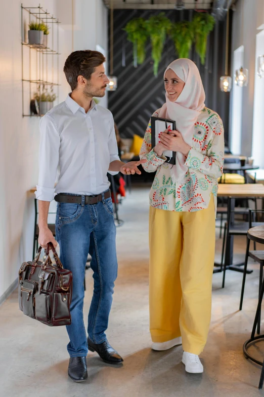 a man and a woman standing next to each other, by Zahari Zograf, trending on pexels, holding a gold bag, ready for a meeting, young middle eastern woman, wearing pants