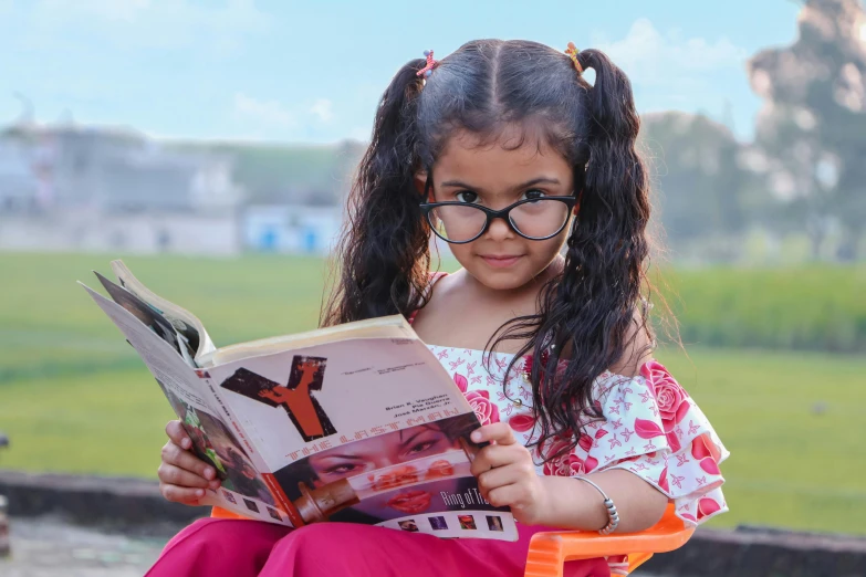 a little girl sitting in a chair reading a book, pexels contest winner, with square glasses, indian girl with brown skin, avatar image, college