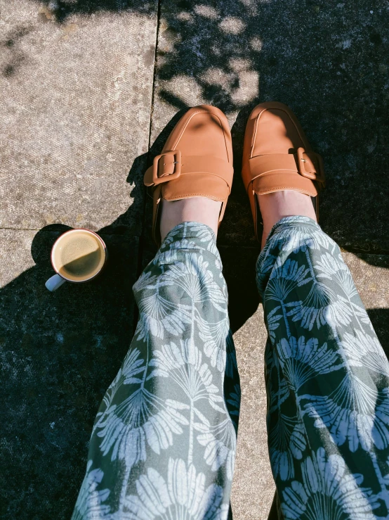 a person standing on a sidewalk next to a cup of coffee, inspired by Balthus, happening, birkenstock sandals, with hawaiian shirt, olive green slacks, shot from roofline