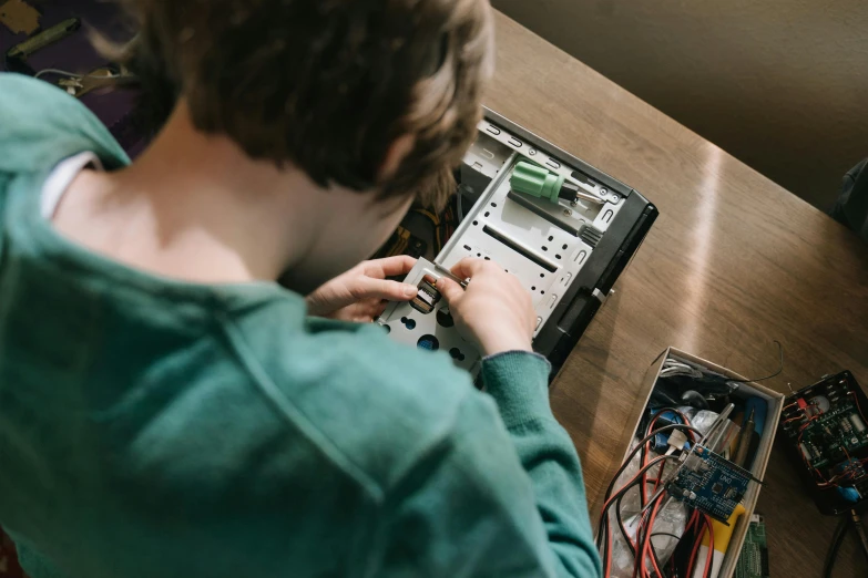 a person sitting at a table working on a computer, by Matthias Stom, pexels contest winner, kids, motherboard, aged 13, thumbnail