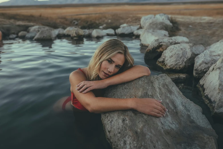 a woman laying on a rock in a body of water, looking smug, blonde women, paul barson, 2019 trending photo