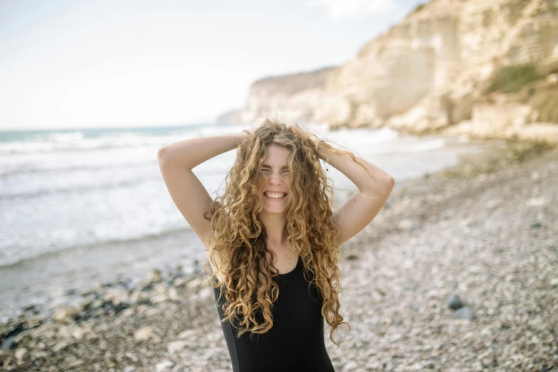 a woman standing on top of a beach next to the ocean, a portrait, by Julia Pishtar, pexels contest winner, renaissance, curly middle part haircut, extremely happy, with long hair, portrait of teenage aphrodite