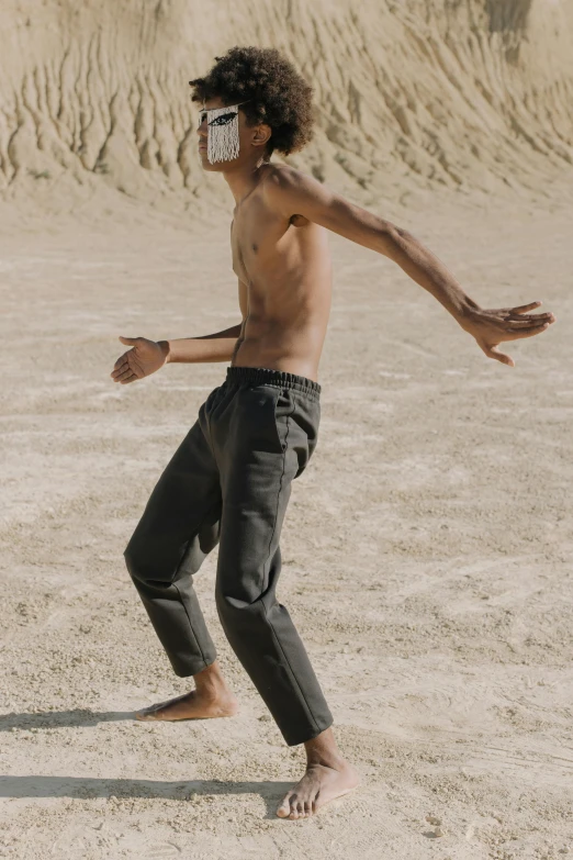 a man that is standing in the sand with a frisbee, by Nathalie Rattner, unsplash, conceptual art, cargo pants, classic dancer striking a pose, thin young male, grey