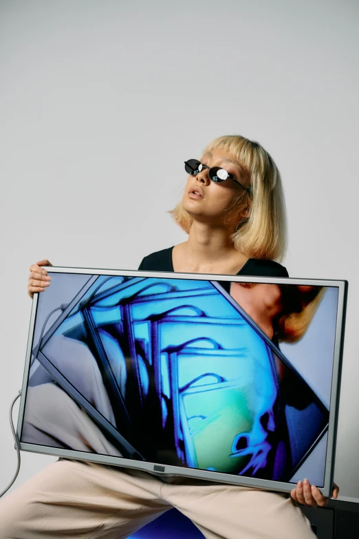 a woman sitting on a chair holding a laptop computer, an album cover, inspired by Gao Cen, unsplash, video art, mirror shades, terry richardson, tv still frame, a blond