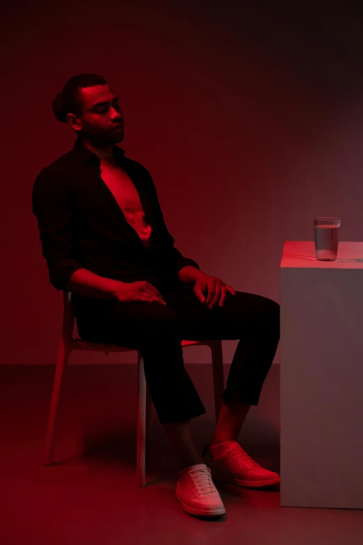 a man sitting on a chair in front of a red light, an album cover, pexels contest winner, neo-figurative, showstudio, dark-skinned, ignant, full body potrait holding bottle