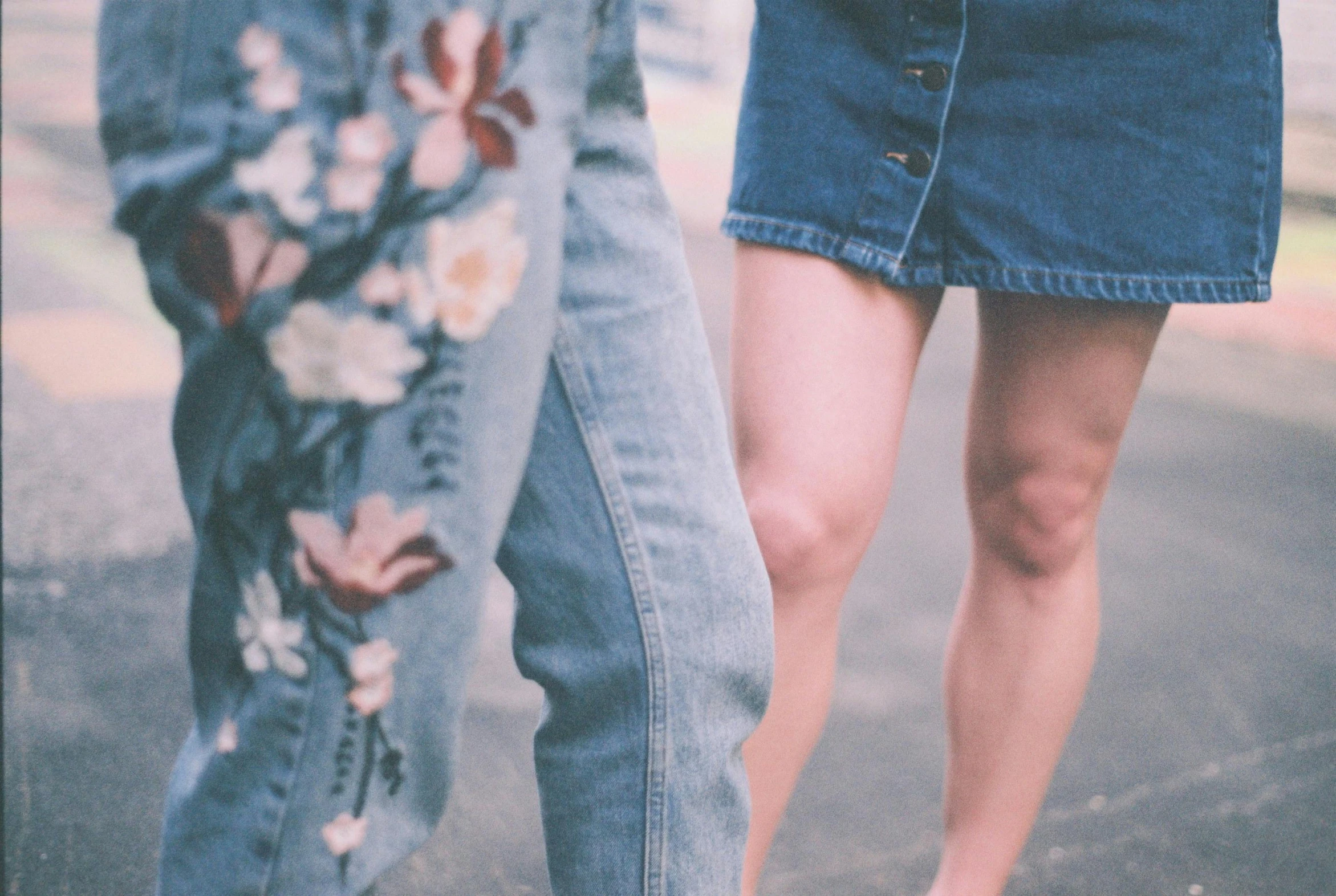 a woman standing next to a man on a skateboard, trending on pexels, antipodeans, wearing denim short shorts, flowers around, walking toward you, woman holding another woman