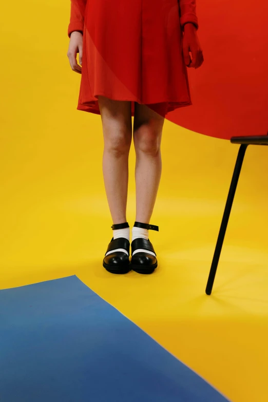 a woman in a red dress standing next to a chair, inspired by Bauhaus, trending on unsplash, slippers, wearing skirt and high socks, black and yellow, panoramic view of girl