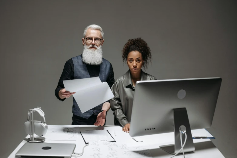 a man and a woman standing in front of a computer, by Adam Marczyński, trending on unsplash, long grey beard, paper, product design shot, on a white table