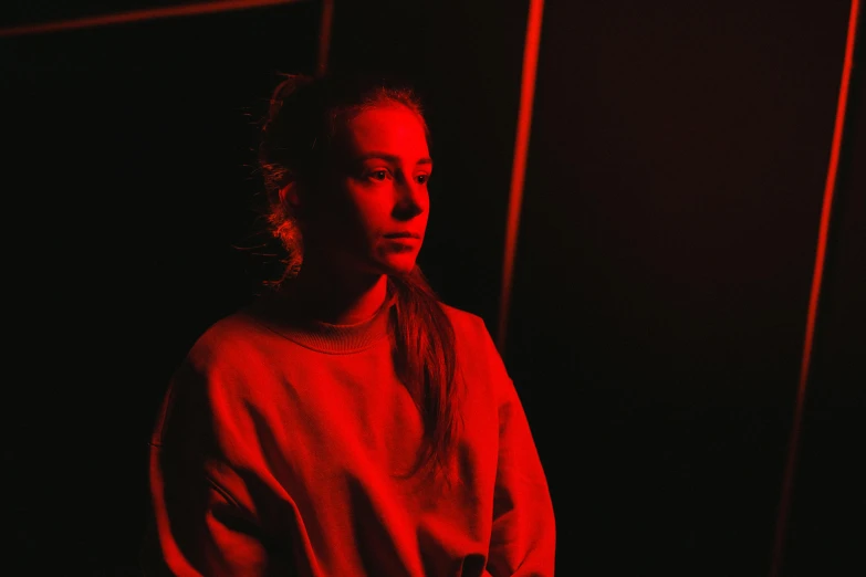 a woman standing in front of a red light, a portrait, pexels contest winner, digital art, dark. studio lighting, portrait sophie mudd, contemplating, sitting down