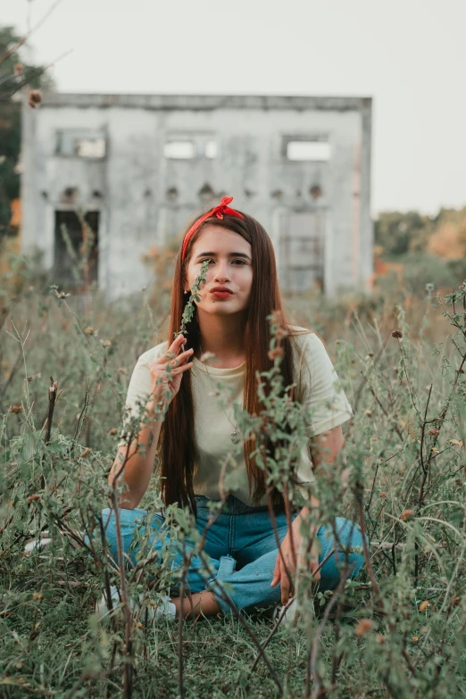 a woman sitting in a field holding a flower, a colorized photo, inspired by Elsa Bleda, pexels contest winner, red bow in hair, standing in abandoned building, red hair and attractive features, slightly pixelated