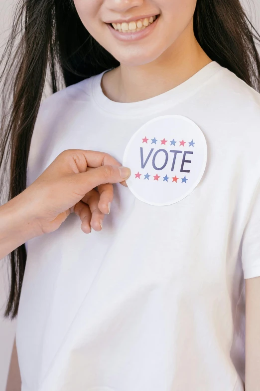 a woman with a vote sticker on her shirt, by Nicolette Macnamara, shutterstock contest winner, for kids, silicone patch design, girl standing, white