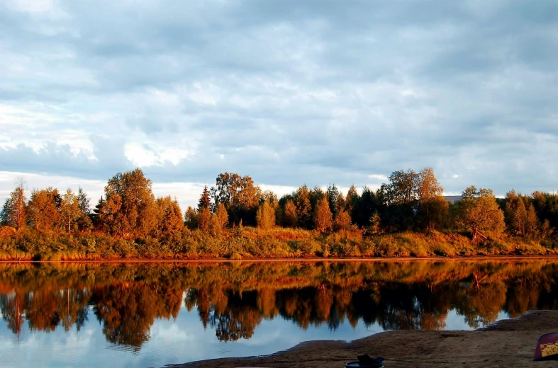 a body of water with trees in the background, hurufiyya, warm colours, puyallup berteronian, on a riverbank, skies behind