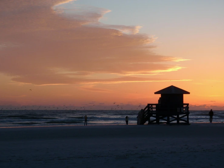 a lifeguard tower sitting on top of a sandy beach, by Kristin Nelson, unsplash contest winner, renaissance, orange sun set, florida, people in beach, the sky is a faint misty red hue