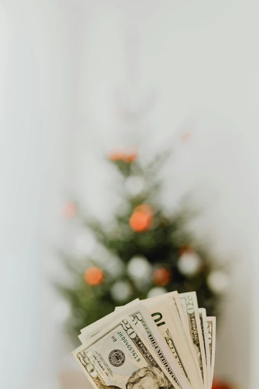 a hand holding a stack of money in front of a christmas tree, a photo, pexels contest winner, modernism, gif, - 6