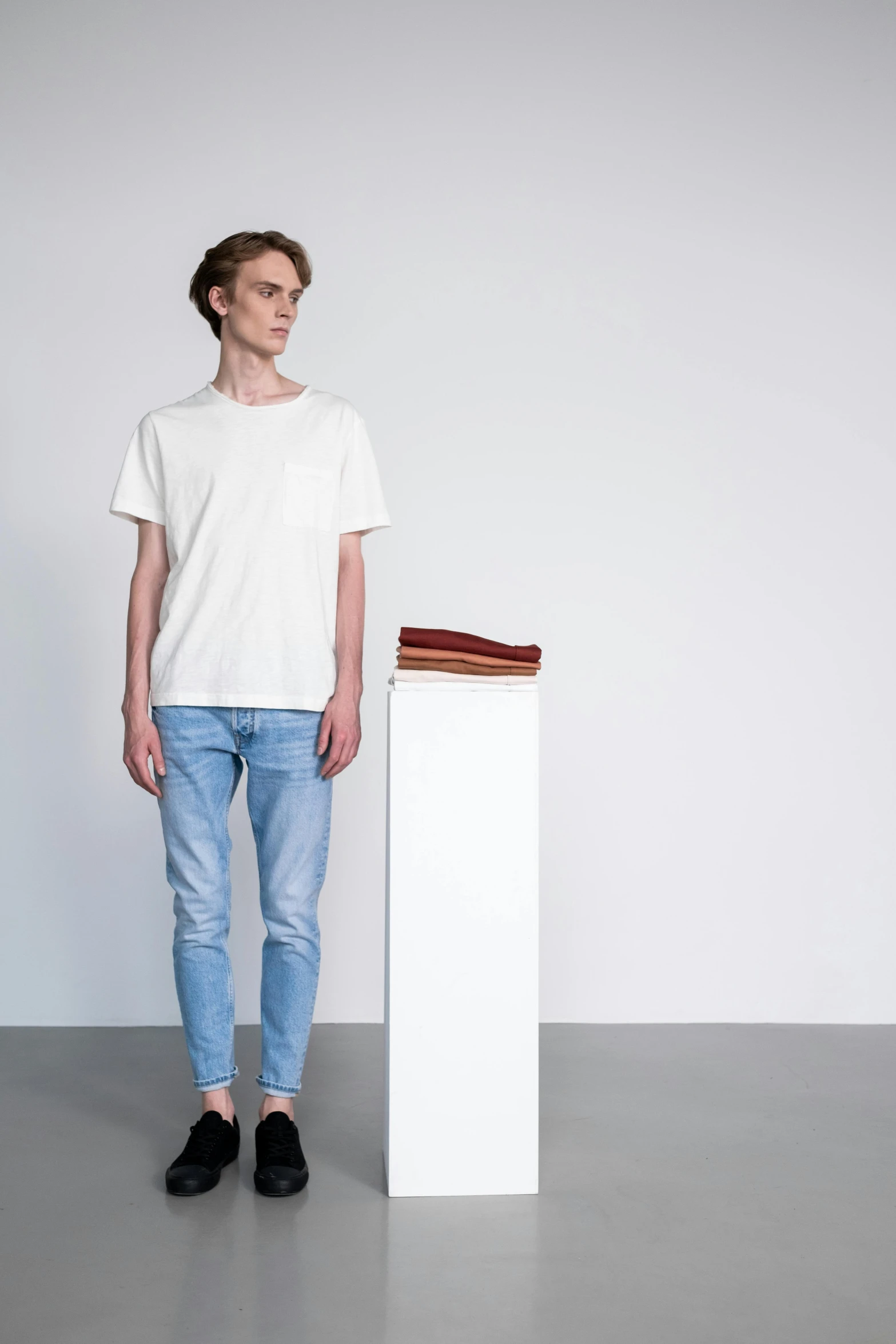 a man standing in front of a white pedestal, by Tobias Stimmer, minimalism, jeans and t shirt, detailed product image, offwhite, small stature