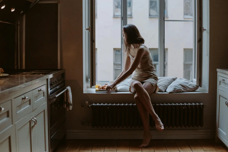 a woman sitting on a window sill in a kitchen, inspired by Elsa Bleda, pexels contest winner, sitting on edge of bed, sleepy feeling, afternoon hangout, short in stature