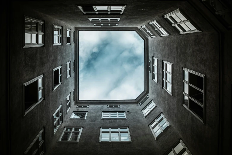 a very tall building with lots of windows, an album cover, inspired by André Kertész, unsplash contest winner, a wide open courtyard in an epic, looking up onto the sky, portal to another world, square