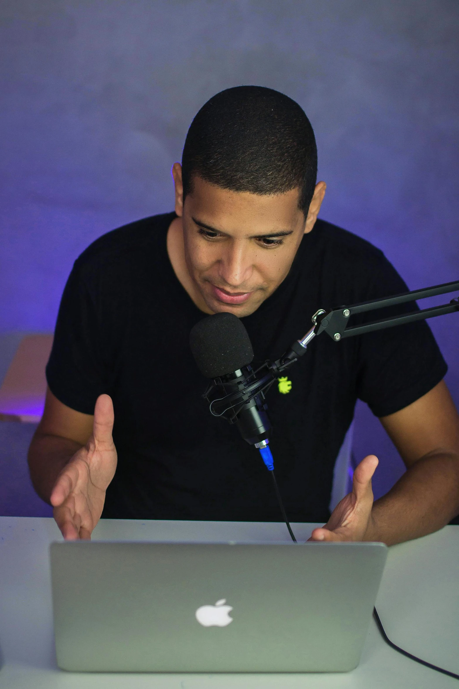 a man sitting in front of a laptop computer, by Daren Bader, rapping into microphone, ronaldo nazario, in a dark studio room, he is wearing a black t-shirt