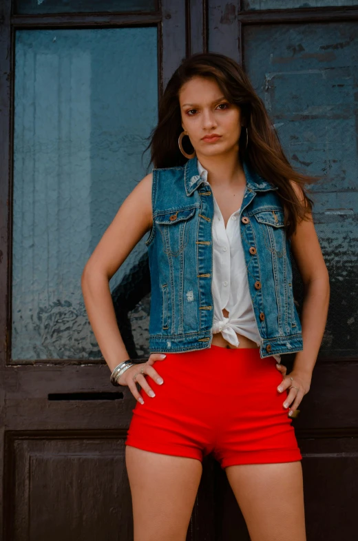 a woman standing in front of a wooden door, an album cover, inspired by Elsa Bleda, pexels contest winner, wearing red shorts, outfit : jeans and white vest, headshot, portrait rugged girl