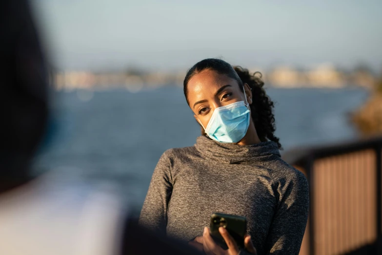 a woman wearing a face mask looking at her phone, a picture, trending on pexels, happening, near a jetty, health supporter, african american woman, bay area