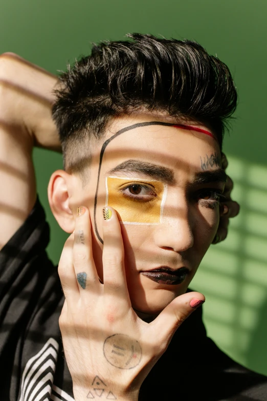 a man standing in front of a green wall, an album cover, inspired by Hedi Xandt, trending on pexels, yellow makeup, stripe over eye, asian man, androgynous
