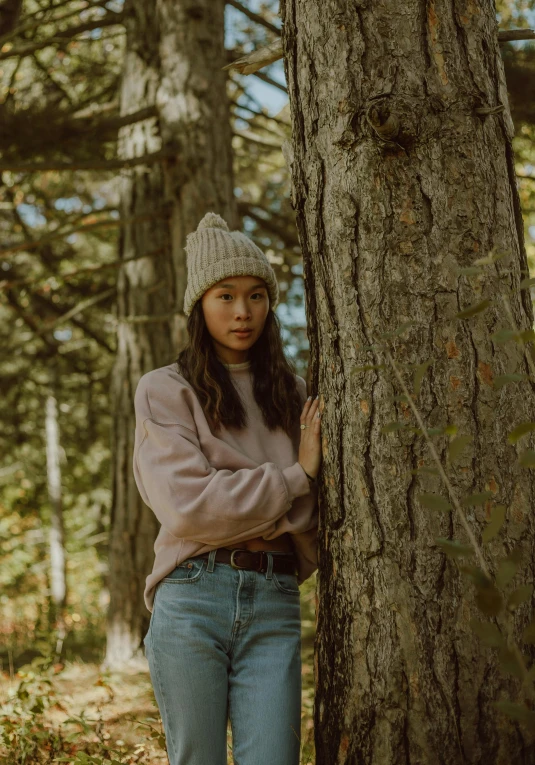 a woman leaning against a tree in the woods, by Andrew Stevovich, unsplash contest winner, wearing casual sweater, asian descent, wearing farm clothes, wearing beanie