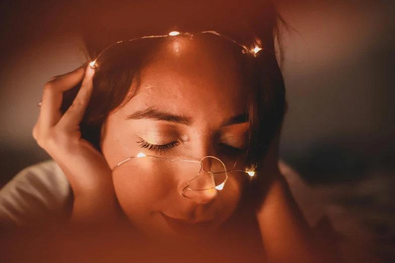 a close up of a person with glasses on, trending on pexels, magical realism, fairy lights, orange halo around her head, sleepy feeling, glowing - thin - wires