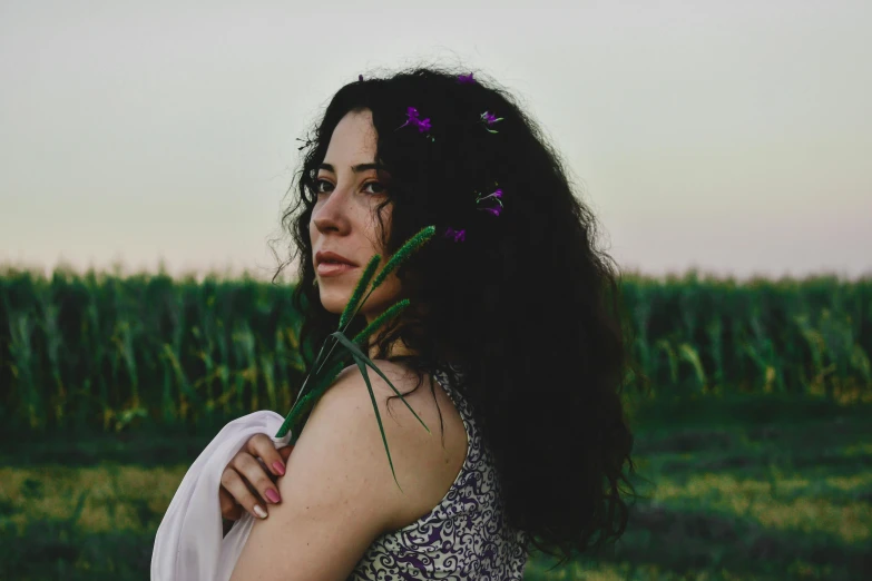 a woman standing in a field with a flower in her hair, an album cover, inspired by Elsa Bleda, pexels contest winner, renaissance, curly dark hair, violet myers, ((portrait)), profile image