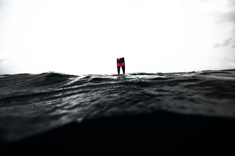 a person standing on a surfboard in the middle of the ocean, a picture, unsplash, purism, wearing a black and red suit, nicolas delort, worried, tiny details
