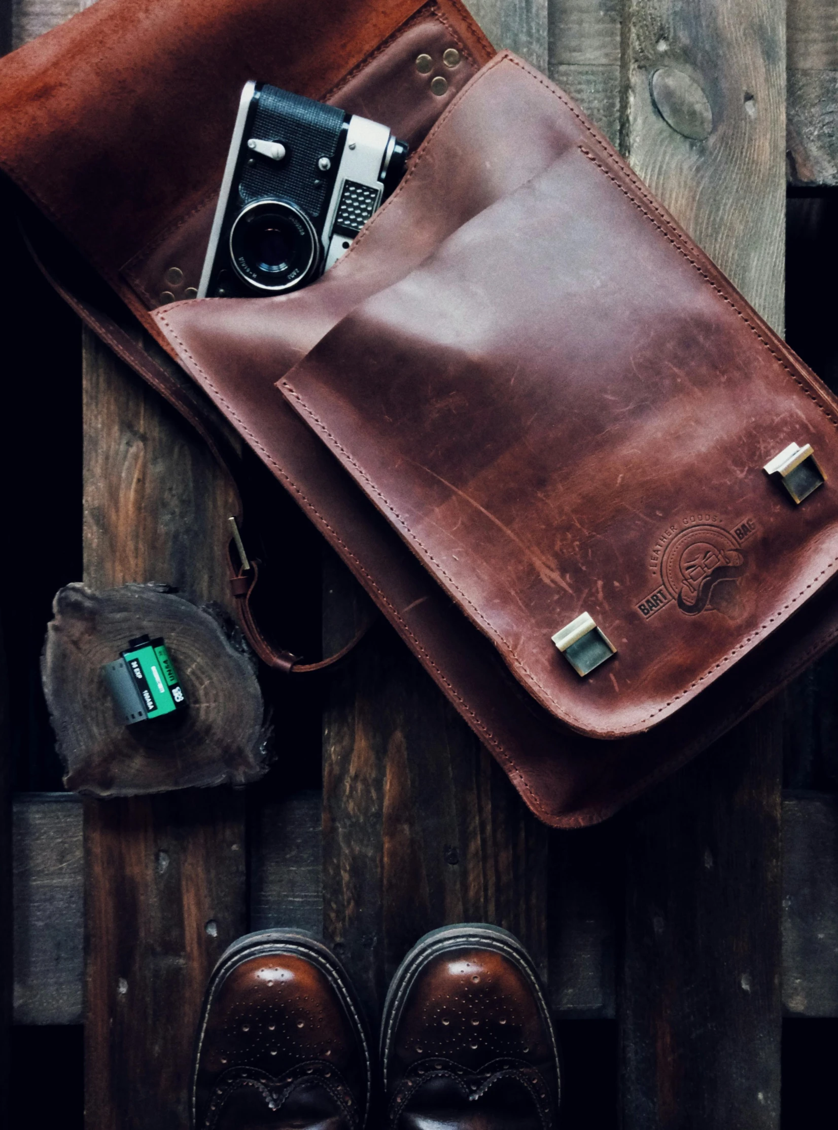 a brown bag sitting on top of a wooden floor next to a pair of shoes, inspired by Elsa Bleda, unsplash, vintage camera, high detailed close up of, wearing leather, rugged ranger