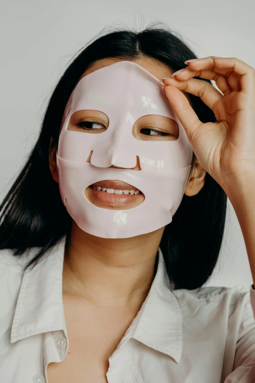 a woman putting a mask on her face, wide forehead, smiling into the camera, silicone skin, with no face