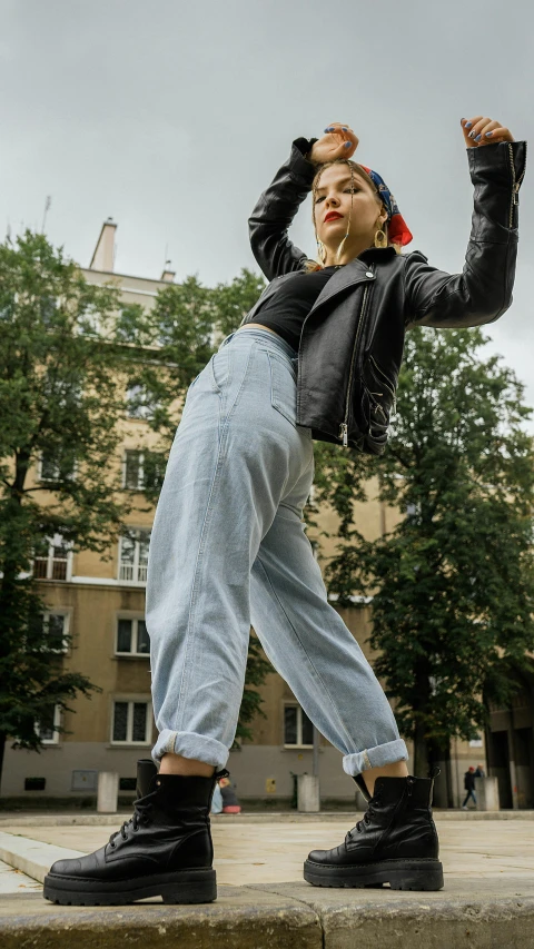 a woman in black jacket and jeans standing on steps, an album cover, by Anna Katharina Block, trending on pexels, baggy pants, eighties-pinup style, in an action pose, 2708519935