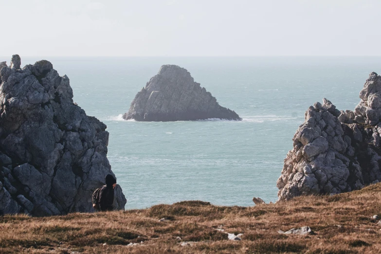 a group of people standing on top of a hill next to the ocean, by Rachel Reckitt, unsplash contest winner, big sharp rock, distant hooded figures, three views, pembrokeshire