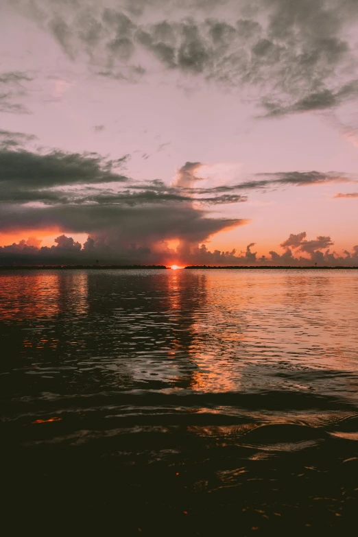 the sun is setting over a body of water, by Daniel Seghers, trending on vsco, post processed 4k, rain lit, tropical atmosphere
