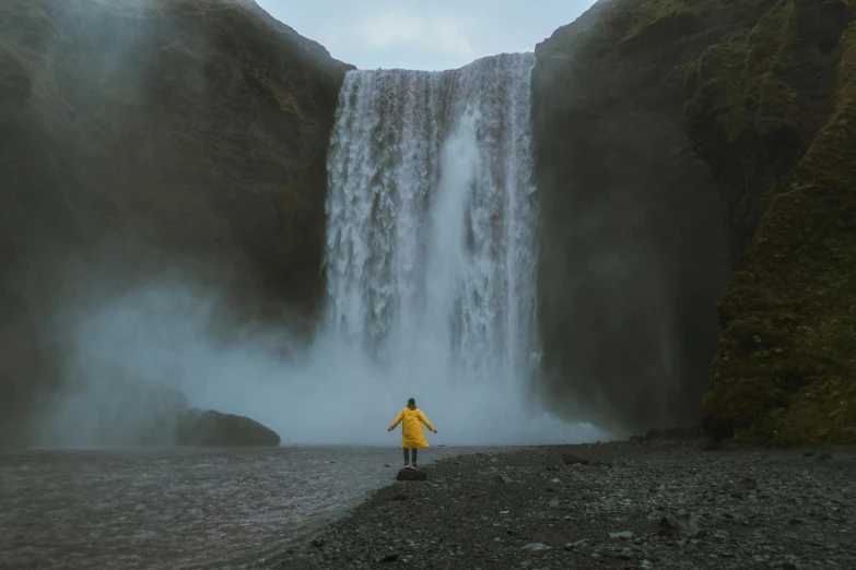 a person standing in front of a waterfall, pexels contest winner, national geographics, nostalgic 8k, flowing cape, drenched clothing