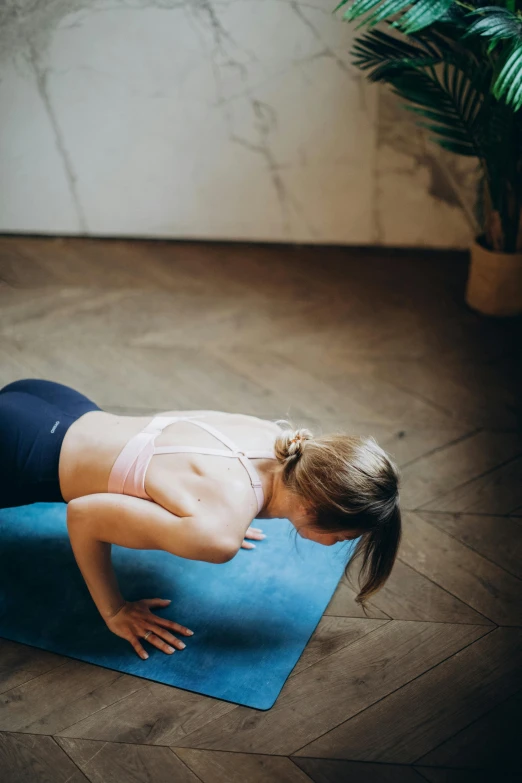 a woman doing a yoga pose on a blue mat, by Adam Marczyński, pexels contest winner, tight push up bra, at home, gif, looking down