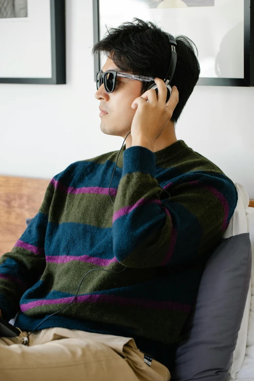 a man sitting on a bed talking on a cell phone, inspired by Oka Yasutomo, unsplash, visual art, striped sweater, wearing shades, detail shot, wearing headset