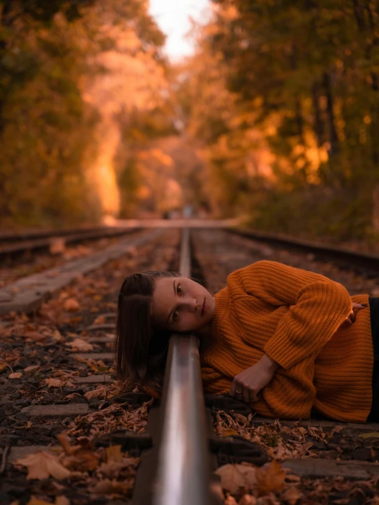 a woman laying down on a train track, inspired by Elsa Bleda, unsplash contest winner, realism, 🍂 cute, 2019 trending photo, orange glow, single portrait