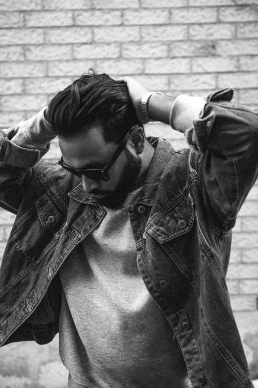 a man standing in front of a brick wall, a black and white photo, inspired by Camilo Egas, pexels, denim jacket, topknot, wearing shades, ray william johnson