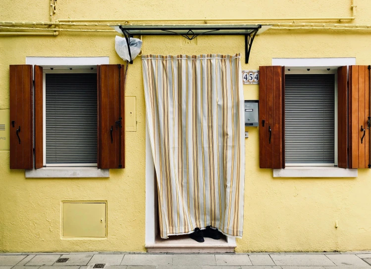 a red fire hydrant sitting in front of a yellow building, an album cover, by Carey Morris, unsplash, hyperrealism, curtains, venice biennale, stripes, doorway