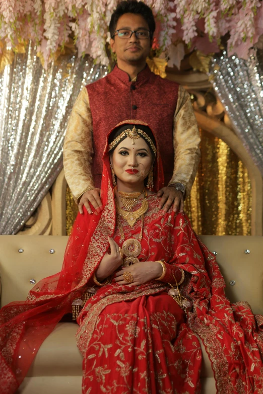 a man and a woman sitting on a couch, hurufiyya, wearing a wedding dress, bangladesh, red and golden color details, thumbnail