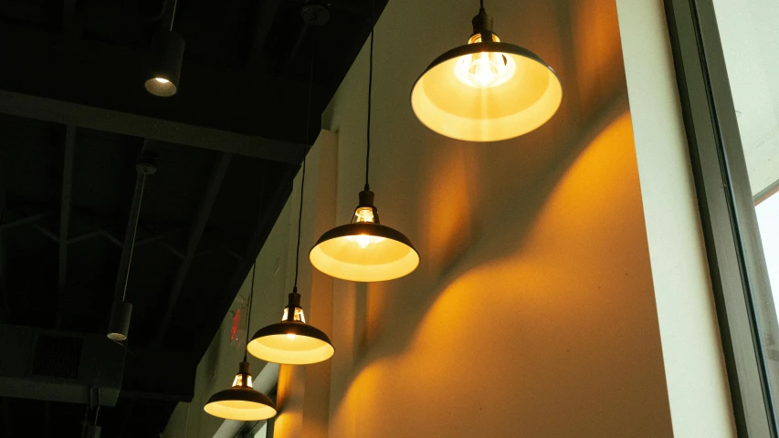 a row of lights hanging from the side of a wall, warm yellow lighting, commercial lighting, cafe lighting, overhead light